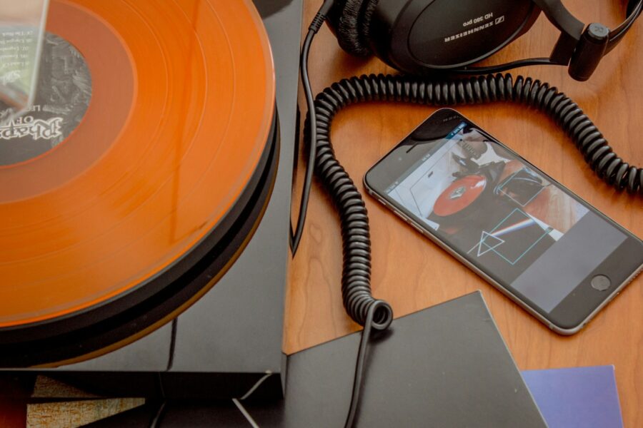 Plokštelių grotuvas, vinilo albumai ir šalia padėtas telefonas su muzikos programėle