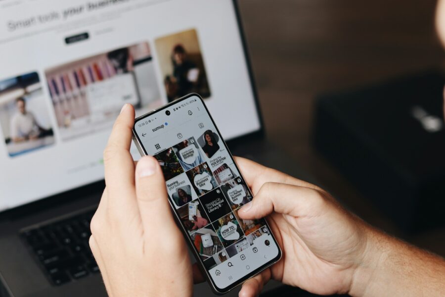 Jaunuolis naršo socialiniuose tinkluose ir žiūri lietuviškus memus telefone bei nešiojamajame kompiuteryje