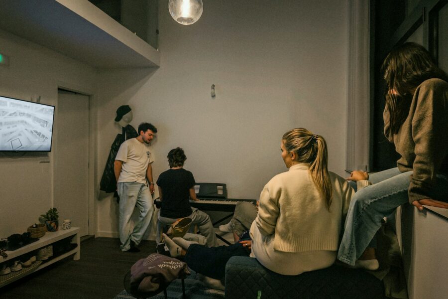 Draugų kompanija žiūri komediją namuose, ant sofos dalijasi spragėsiais ir juoku